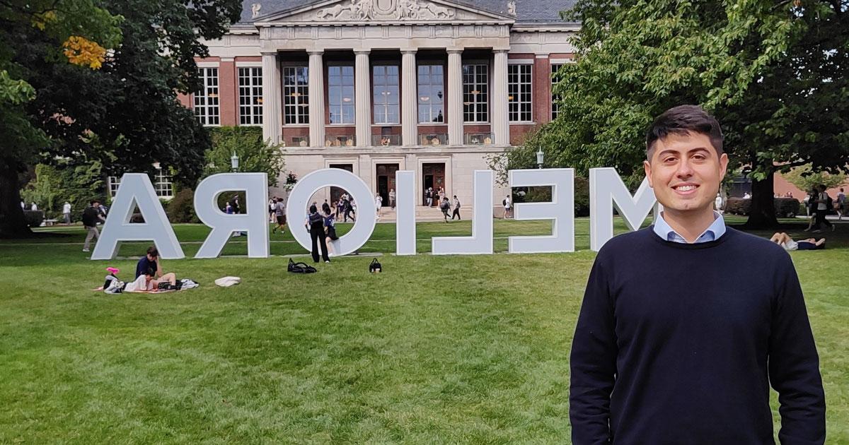 Alexis Sparapani poses for a photo on the University of Rochester campus in front of a display that reads: "Meliora".